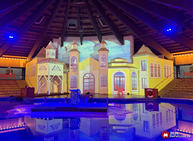 Aquarena im Hansa-Park mit gelb beleuchteter Bühnenkulisse, Wasserbecken und hölzernem Steg unter blauem Licht