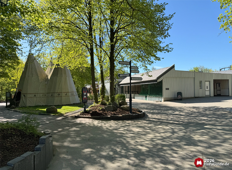 Sonniger Frühlingstag im Hansa-Park mit Blick auf zwei große Tipis im Abenteuerland, umgeben von grünen Bäumen und einem hellen Gebäude im Hintergrund