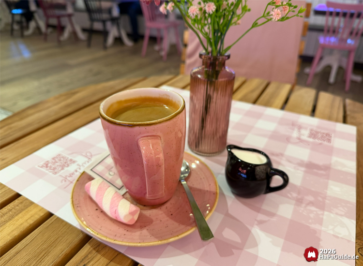 Tasse Kaffee in rosa Geschirr mit Marshmallow und Milchkanne auf Holztisch im Café Rosa des Hansa-Parks