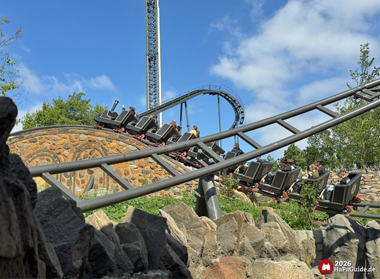 Zug der Cornwall Coaster Achterbahn im Hansa-Park fährt über einen Hügel aus Steinen, im Hintergrund die Strecke von Nessie und der Highlander-Turm