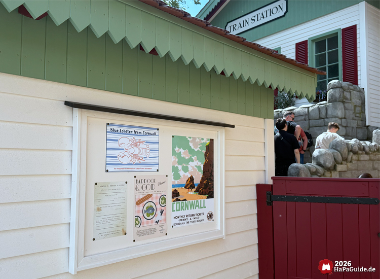 Tourist Info Gebäude am Ausgang des Cornwall Coaster im Hansa-Park mit grüner Dachverkleidung und Plakaten zu Cornwall, darunter 'Blue Lobster from Cornwall' und 'Haddock & Cod'