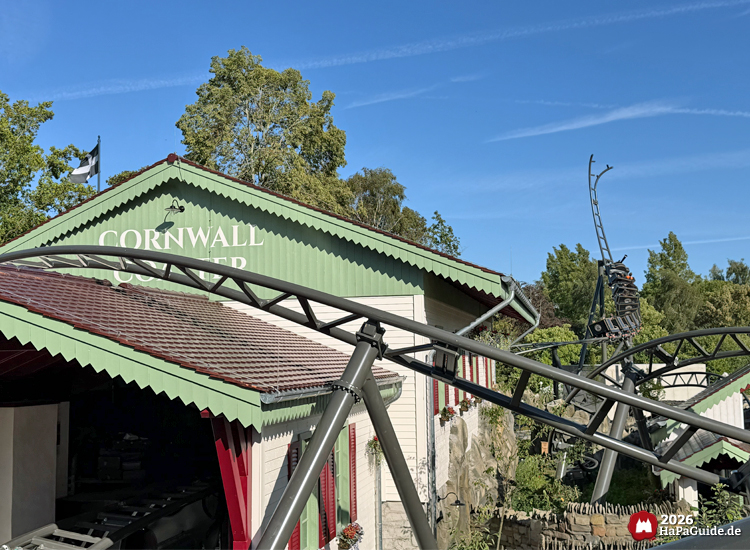 Station der Cornwall Coaster Achterbahn im Hansa-Park mit grünem Giebel und rotem Dach, Zug fährt aus der Halle heraus auf den Spike, im Hintergrund die geschwungene Stahlstrecke