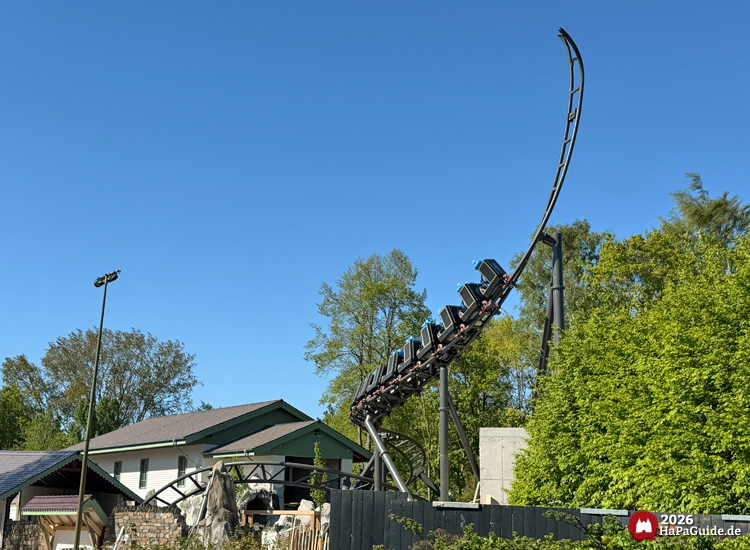 Cornwall Coaster im Hansa-Park: Achterbahnzug mit blauen Testdummies auf Sitzen fährt steil nach oben auf schwarzem Spike vor hellen Gebäuden und grünen Bäumen unter klarem Himmel, Foto Mai 2026 von HaPaGuide.de