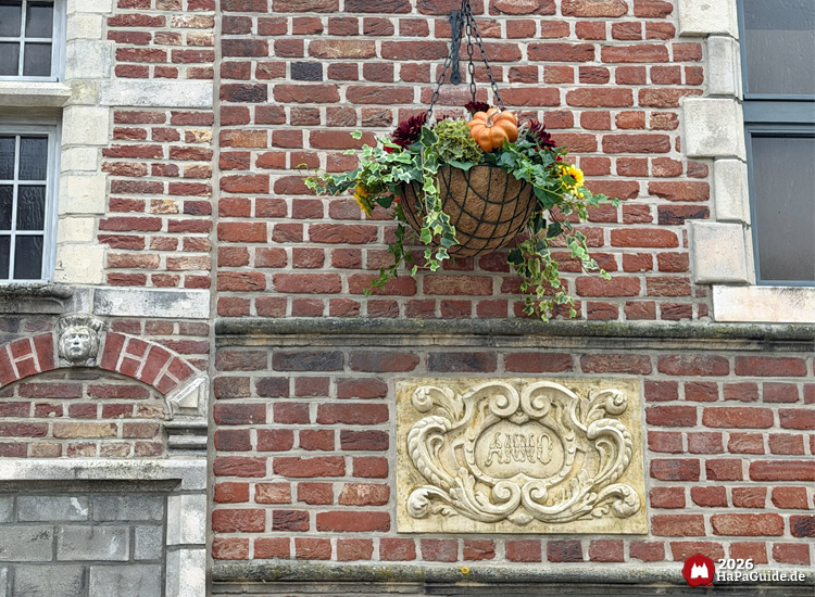 Herbstliche Blumenampel mit Kürbis, Efeu und Chrysanthemen an roter Backsteinfassade des Hanse-Kontors im Hansa-Park, darunter Steinrelief mit Schriftzug Anno