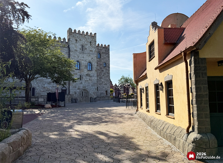Blick entlang eines gepflasterten Wegs im Hansa-Garten des Hansa-Park mit dem Palacio de Braga auf der linken Seite und gelbem Gebäude mit rotem Dach am Carrousel Baltique auf der rechten Seite