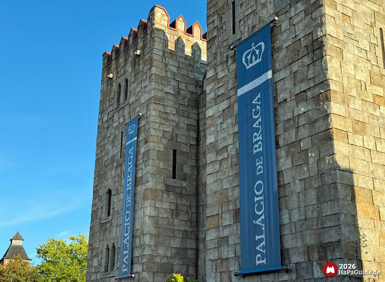 Zwei Türme des Palacio de Braga im Hansa-Park mit grauer Steinfassade und blauen Bannern mit weißer Krone und Schriftzug Palácio de Braga, klarer blauer Himmel im Hintergrund