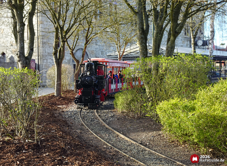 Parkeisenbahn Hansa-Park Express mit Dampflok fährt durch begrünte Landschaft, Fahrgäste in offenen Waggons