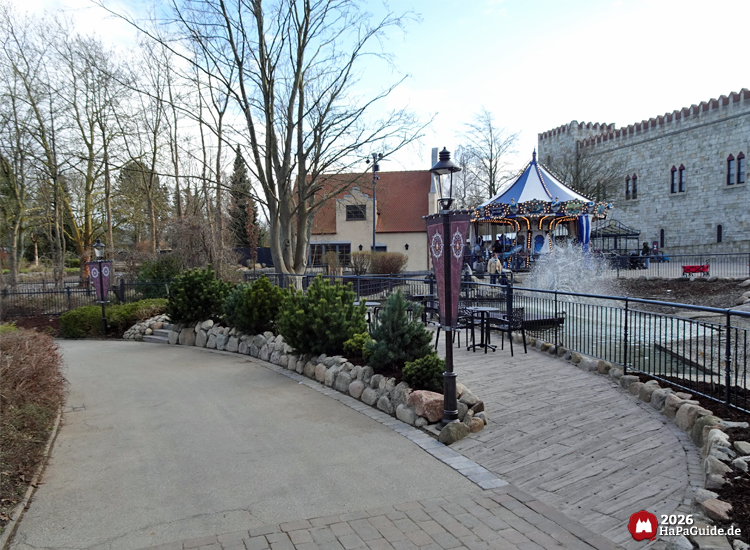 Themenpark Szene mit Brunnen, Außenterrasse und beleuchtetem Karussell vor portugiesischer Burg Palacio de Braga im Hansa Park