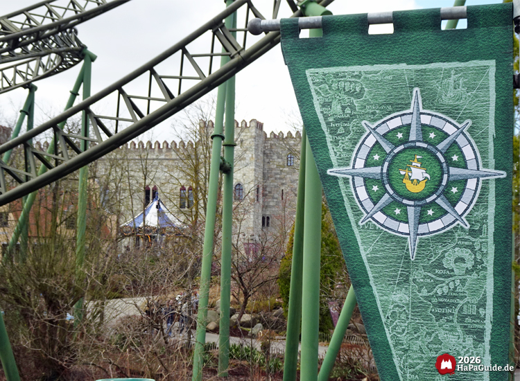 Grünes Banner mit Kompassmotiv unter Buchtknoten der Flucht von Novgorod vor Palacio de Braga im Hansa Park