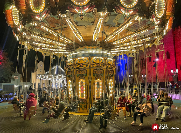 Hanse-Flieger - Fahrgäste warten bei Dunkelheit unter dem beleuchteten Karusselldach
