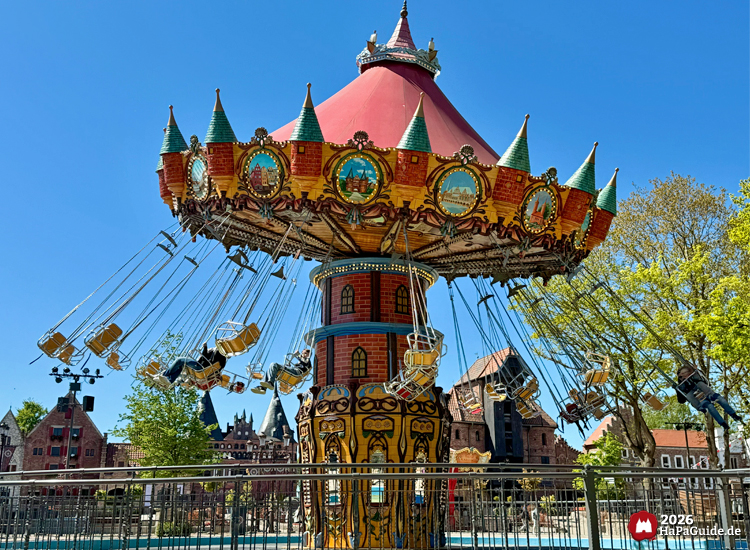 Großes Kettenkarussell Hanse-Flieger im Hansa-Park mit rotem Dach, grünen Turmspitzen und goldenen Ornamenten, im Hintergrund historische Hansefassaden unter klarem blauen Himmel
