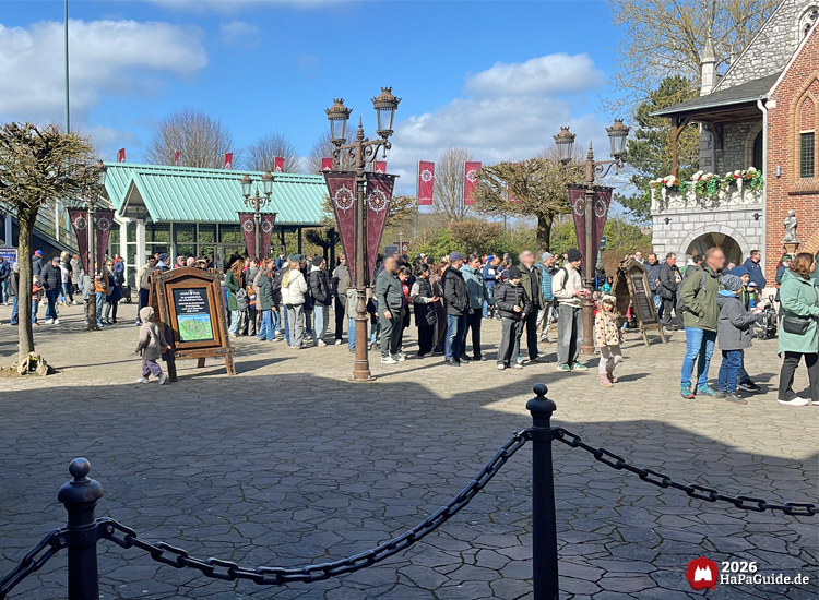 Menschenmenge am Eingang des Hansa-Parks mit historischen Laternen und lila Bannern, Besucher stehen in einer langen Schlange vor dem Holstentor bei sonnigem Wetter