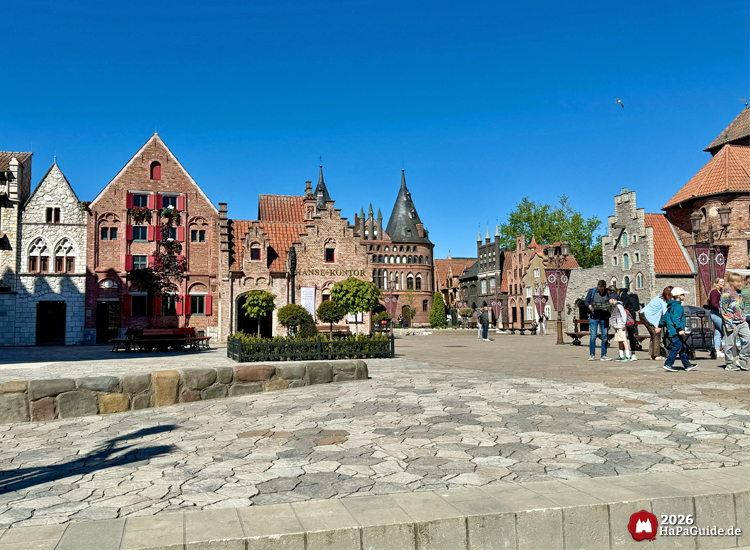 Weitläufiger Platz innerhalb der Hanse in Europa im Hansa-Park mit historischen Gebäuden im Stil der Hansezeit, roten Ziegeldächern und Türmen, Besuchende spazieren über den gepflasterten Platz bei Sonnenschein