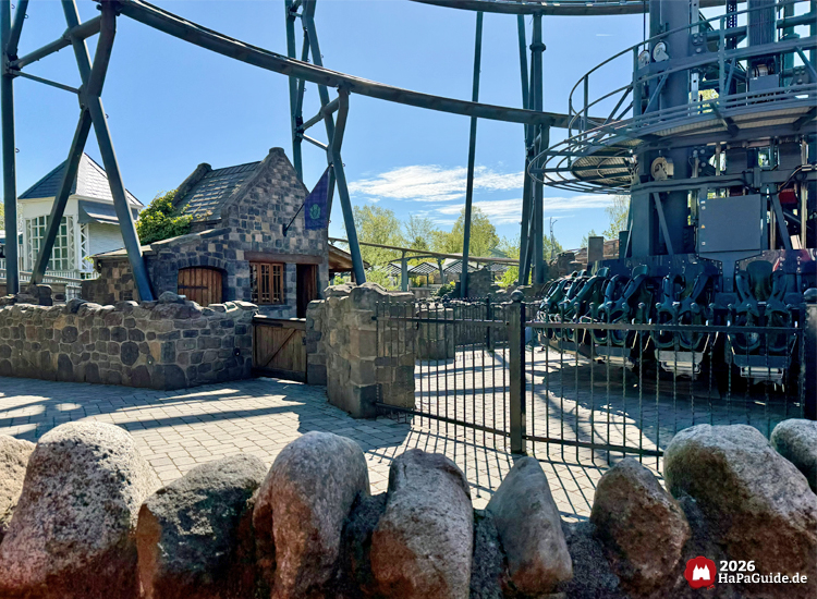 Steinbau im Burgen Stil neben dem Highlander-Freifallturm im Hansa-Park mit Sitzreihen und Stahlkonstruktion bei sonnigem Wetter