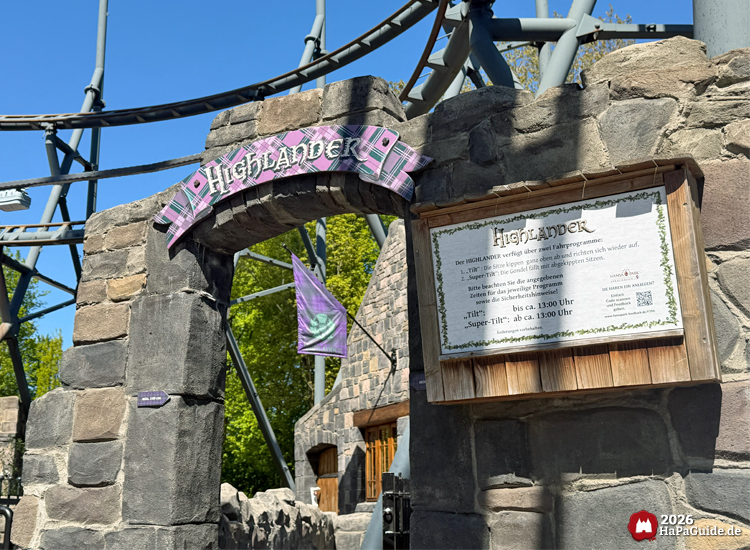 Eingangsbereich der Highlander-Attraktion im Hansa-Park mit steinernem Torbogen, violettem Schild und Informationstafel unter blauem Himmel