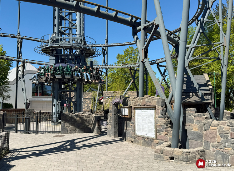 Fahrgäste sitzen im Highlander-Freifallturm im Hansa-Park, umgeben von steinernen Mauern und Stahlkonstruktionen bei sonnigem Wetter