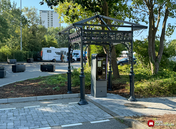 Parkkassenautomat unter verziertem Metalldach auf dem Hansa-Park Parkplatz mit Wohnmobilen im Hintergrund
