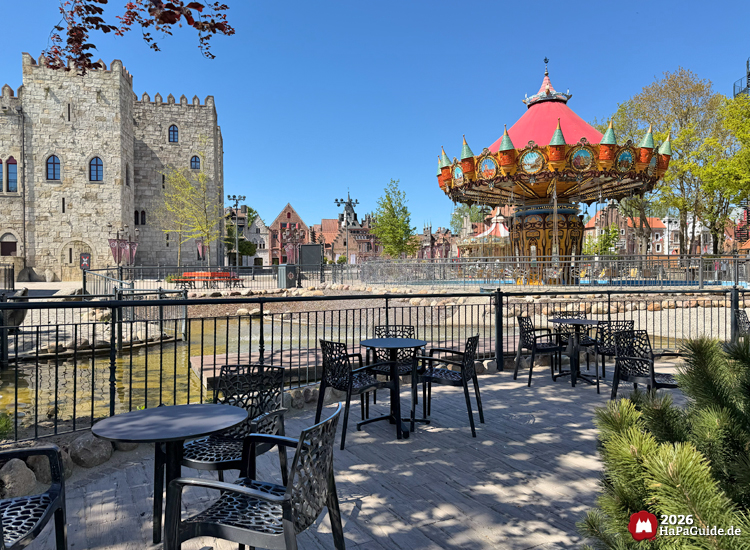 Blick in die Hanse in Europa im Hansa-Park mit Hanse-Flieger und Palacio de Braga bei sonnigem Himmel, Sitzbereich mit schwarzen Metalltischen und Stühlen im Vordergrund