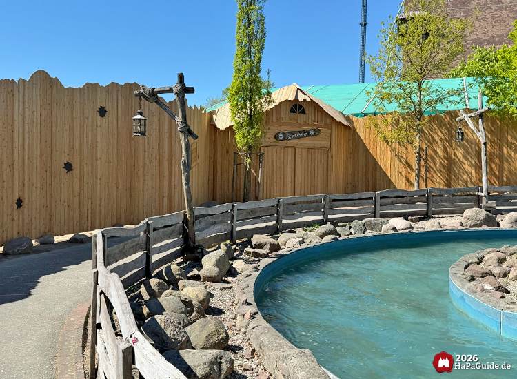 Wasserkanal von Störtebekers Kaperfahrt mit Holzgeländer und maritimer Themenfassade im Hansa-Park, sonniger Frühlingstag mit klarblauem Himmel und grünen Bäumen