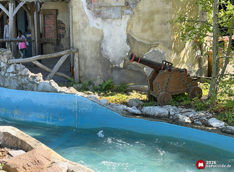 Thematisierte Kanone aus Holz an der Wasserattraktion Störtebekers Kaperfahrt im Hansa-Park, neben verwitterter Burgfassade und blauem Kanal mit fließendem Wasser