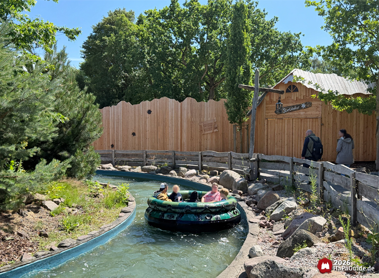 Boot der Wasserattraktion Störtebekers Kaperfahrt im Hansa-Park fährt durch einen Kanal mit Holzbegrenzung, Besucher sitzen im grünen Rundboot, daneben Holzhaus mit Schild 'Störtebeker'
