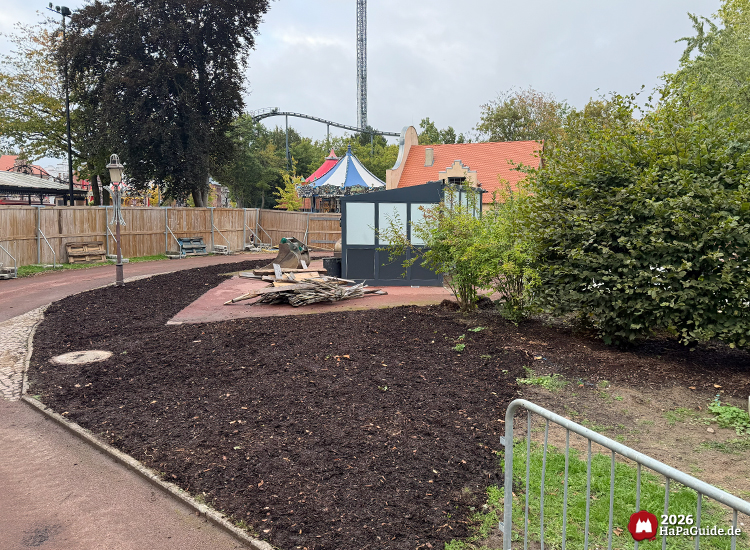 Baubereich des Buddenbrook-Turms im Hansa-Park mit frisch aufgebrachter Erde und kleinem Gebäude des ehemaligen Holsteinturms, dahinter Carrousel Baltique und Nessie, umgeben von Bäumen und Holzzaun