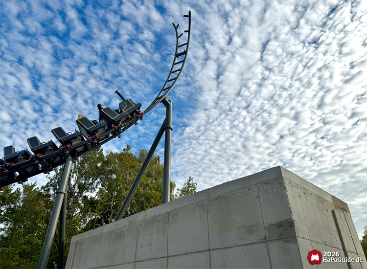 Achterbahn Cornwall Coaster im Hansa-Park mit Zug auf Spike, der abrupt endet, darunter Betonbau und stählerne Stützen, im Hintergrund Bäume und wolkiger Himmel