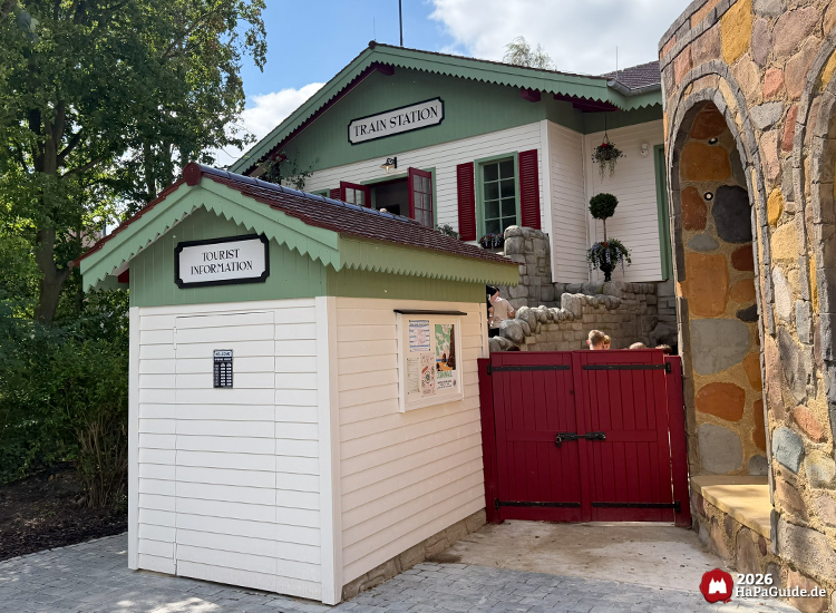 Tourist Information Gebäude der Cornwall Coaster Achterbahn im Hansa-Park mit weißen Wänden, grüner Dachkante und roten Fensterläden, daneben Steinmauer und Tor