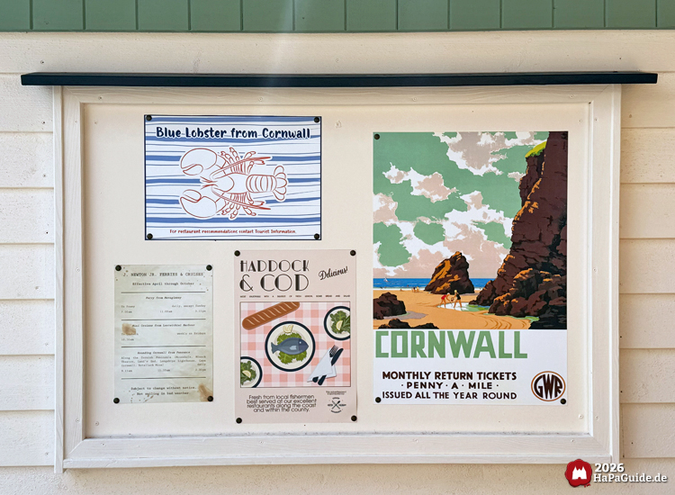 Aushangtafel an der Cornwall Coaster Tourist Information im Hansa-Park mit Plakaten zu Cornwall, darunter 'Blue Lobster from Cornwall', 'Haddock & Cod' und ein Reiseplakat mit Küstenlandschaft