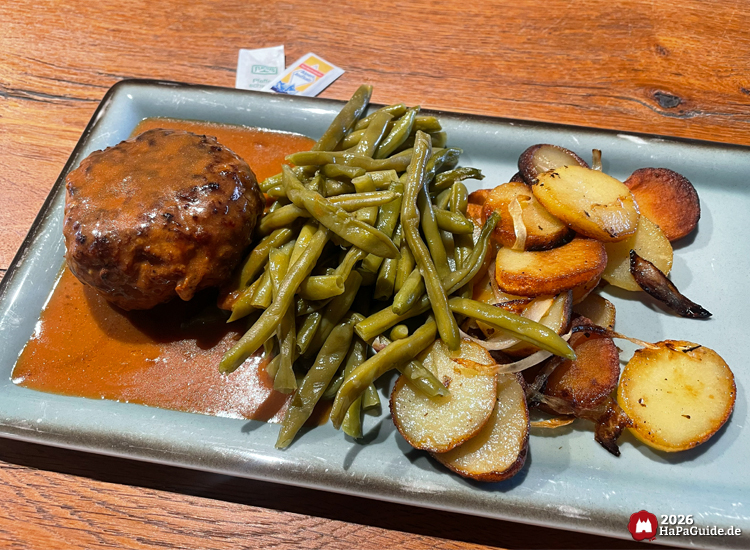 Frikadelle mit Bratkartoffeln und grünen Speckbohnen auf Teller im Restaurant Weltumsegler