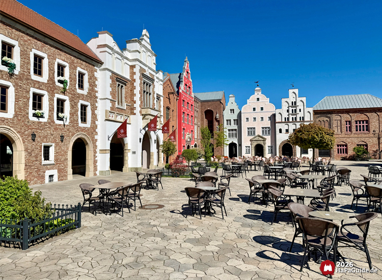 Außenbereich des Hansa-Park Restaurants Weltumsegler mit historischen Fassaden im Stil europäischer Backsteinarchitektur, roten und weißen Giebelhäusern und zahlreichen Sitzplätzen unter blauem Himmel