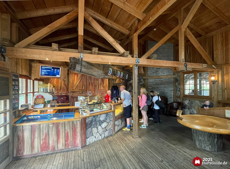 Rustikaler Shop der Crazy Mine im Hansa-Park mit Holz- und Steinoptik, Verkaufstheke mit Eis und Snacks, Besuchende beim Bestellen im gemütlichen Innenraum