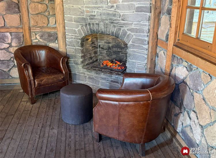 Gemütliche Sitzecke im Hansa-Park Ride-Shop Crazy Mine mit zwei braunen Ledersesseln vor einem Steinofen mit glühenden Kohlen, rustikale Holz- und Steinwand im Hintergrund