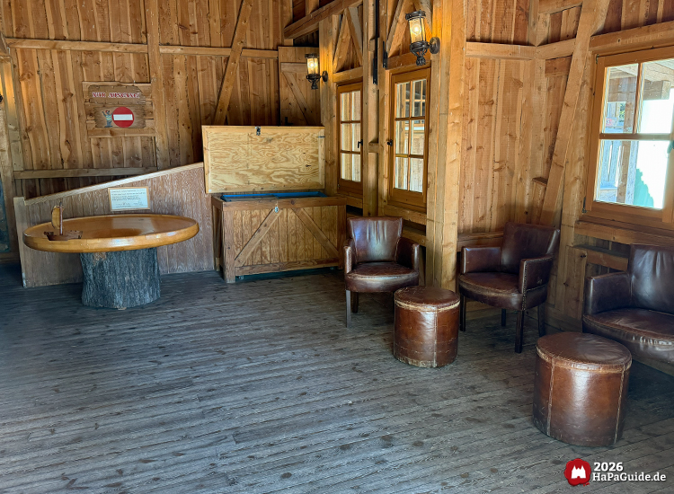 Rustikaler Innenraum im Ride-Shop Crazy Mine im Hansa-Park mit Holzwänden, braunen Ledersesseln und runden Hockern, gemütliche Lounge-Ecke mit warmem Licht und Fensterblick