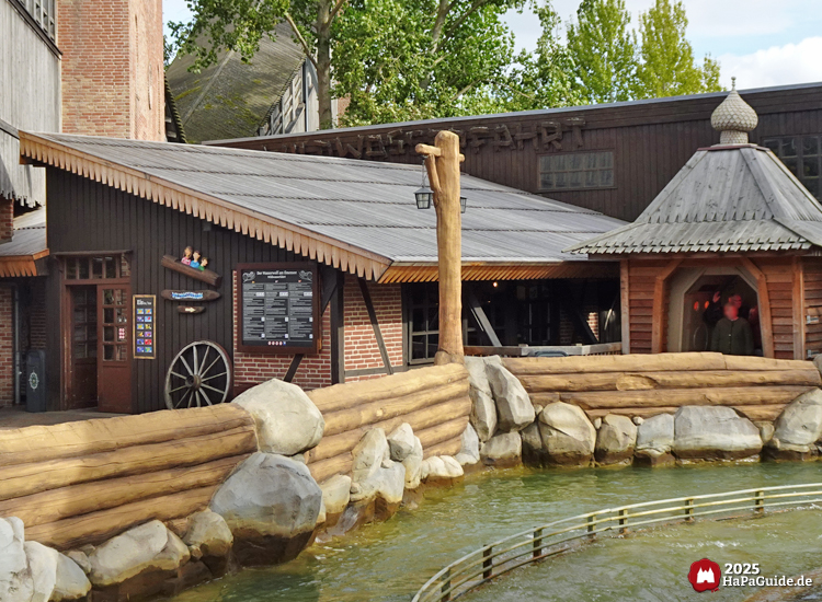 Rustikaler Ride-Shop am Wasserkanal der Wildwasserfahrt im Hansa-Park mit Holzfassade, Wagenrad-Deko und überdachtem Sitzbereich