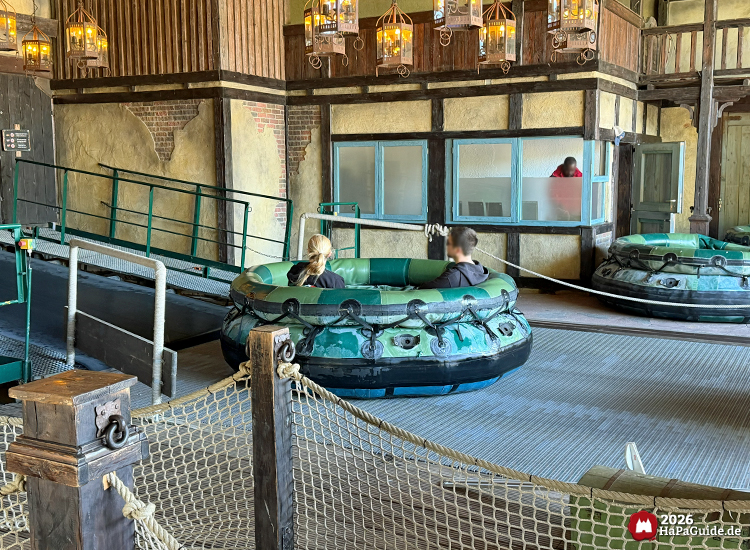 Station des Wasser-Raftings Störtebeker’s Kaperfahrt im Hansa-Park mit Holzverkleidung, Laternen und grünen Rundbooten, Fahrgäste steigen in die Boote unter rustikaler Beleuchtung