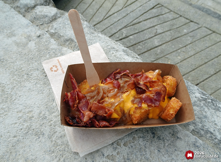 Knusprige Kartoffelrösti mit Käse, Röstzwiebeln und Bacon in einer Pappschale als herzhafter Snack im Bezaubernden Britannien im Hansa-Park