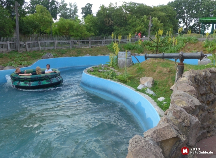 Ein grünes Rundboot passiert eine Wasserkanone