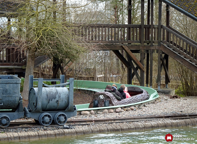 Wildwasserfahrt im Hansa-Park mit vorbeifahrendem Baumstamm-Boot und kleiner Lorenbahn im Vordergrund